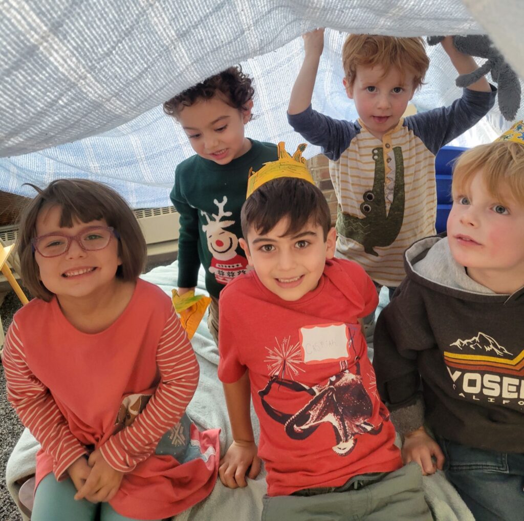 Group of smiling children inside a blanket fort. 