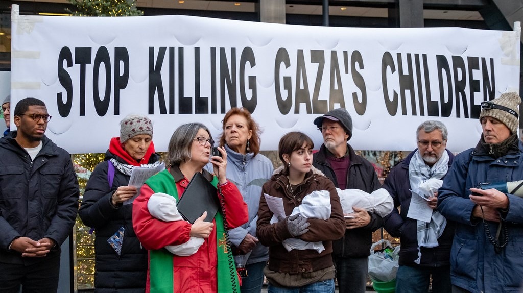 Group of people standing in front of a banner reading "Stop Killing Gaza's Children"