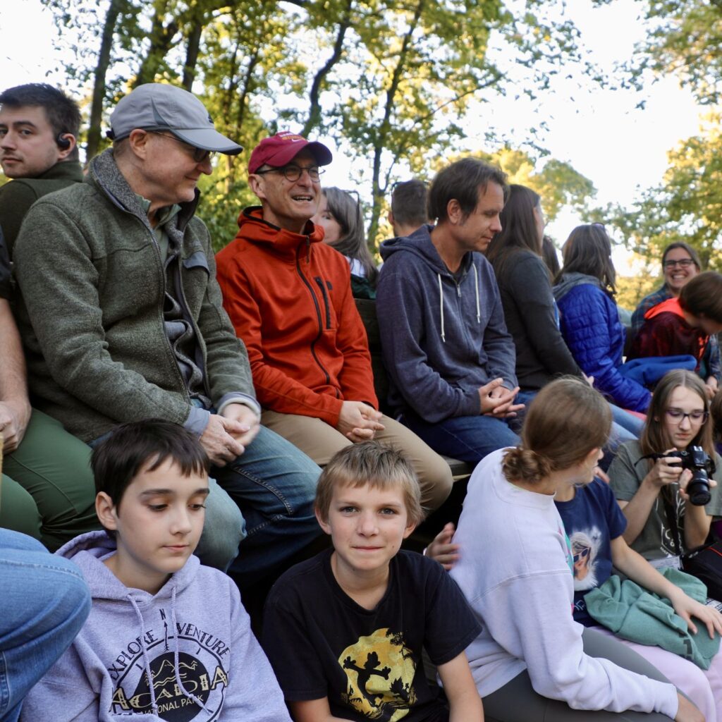 Group of adults and children chatting and laughing on a hayrack ride outside.