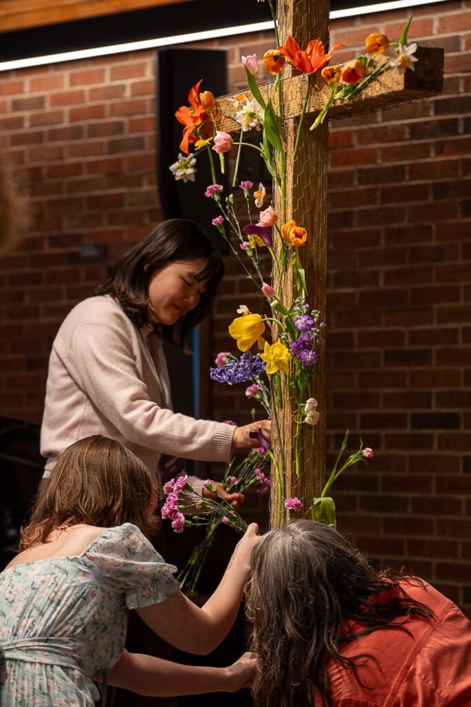 Three women put flowers on a wooden cross