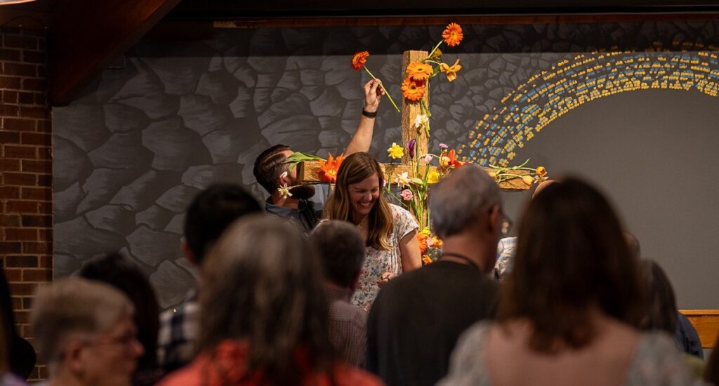 A woman laughing as a man behind her puts a flower on a wooden cross.