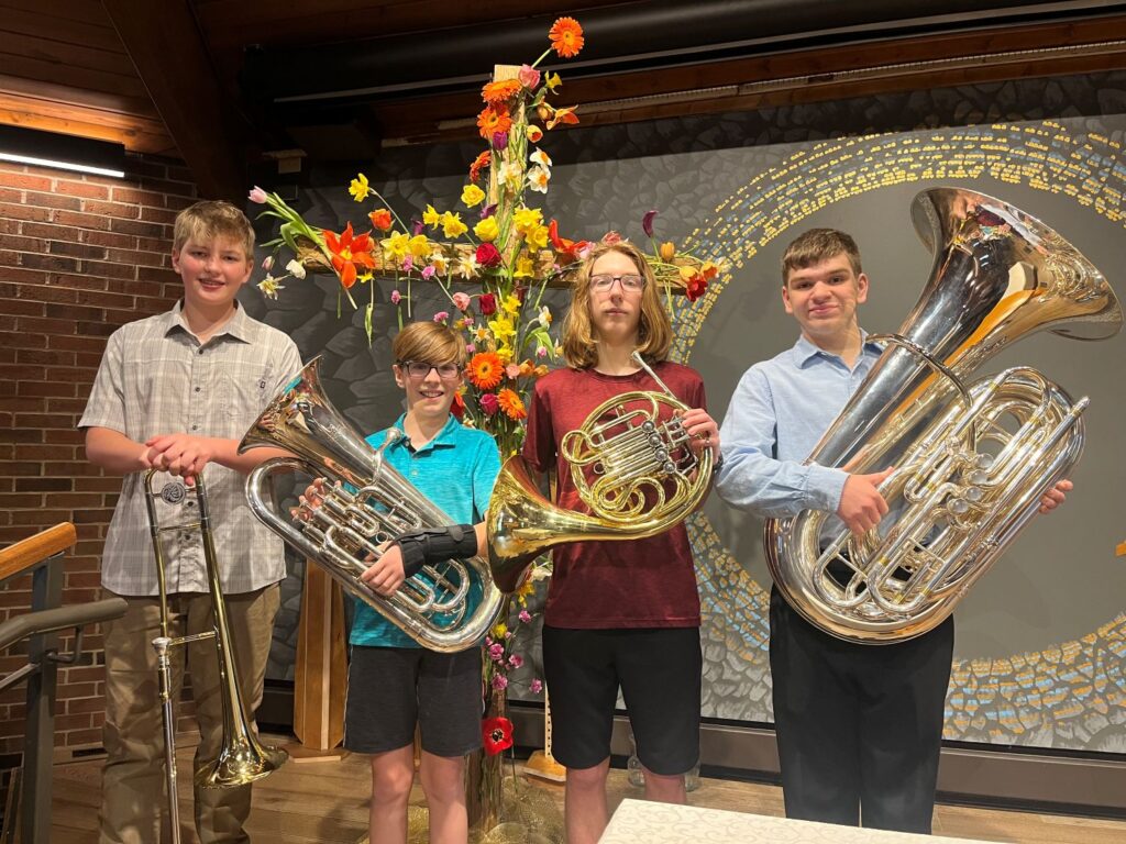 Brass quartet of four male youth inside a church sanctuary.