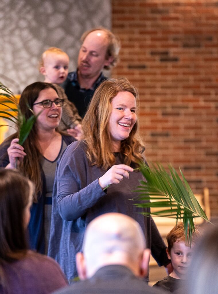 Two women smiling and holding palm leaves inside a sanctuary.