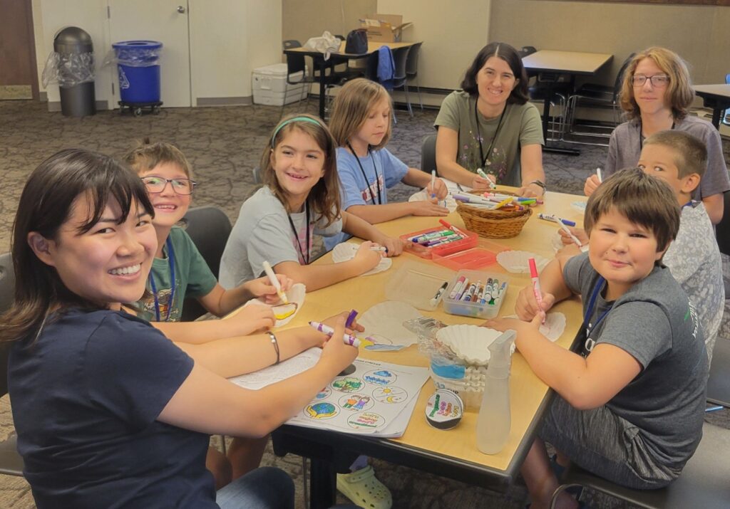 Group of boys and girls enjoy a craft around a table at Vacation Bible School. 