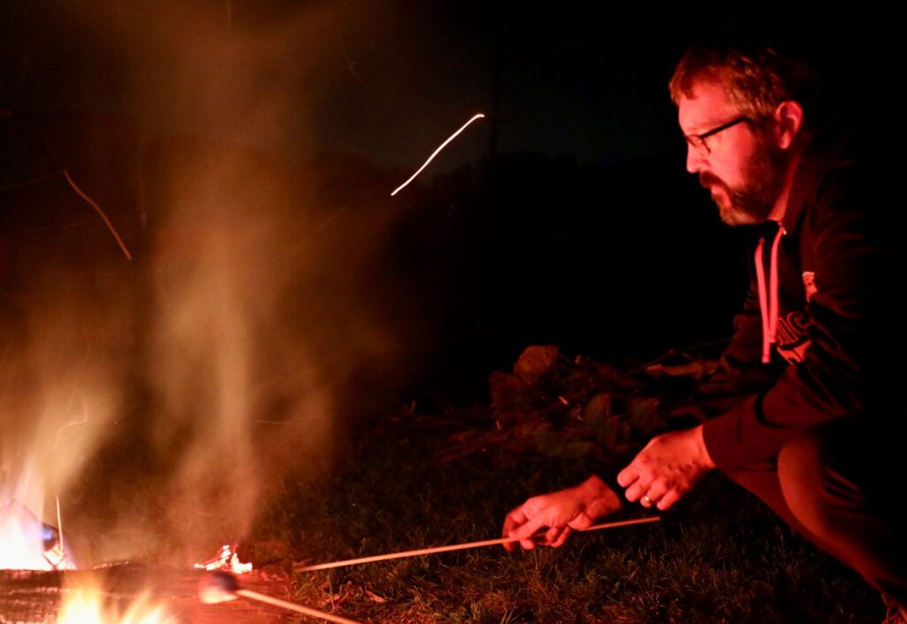 Man roasts a marshmallow over a campfire. 