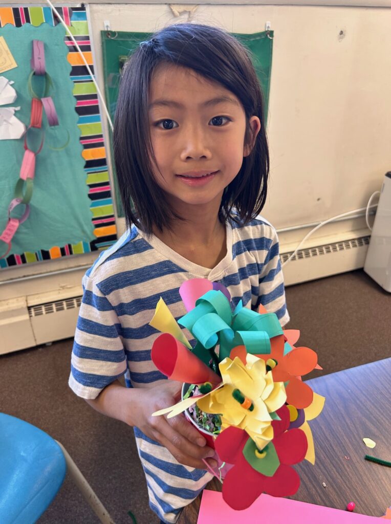 A child holds a flower bouquet made of construction paper. 