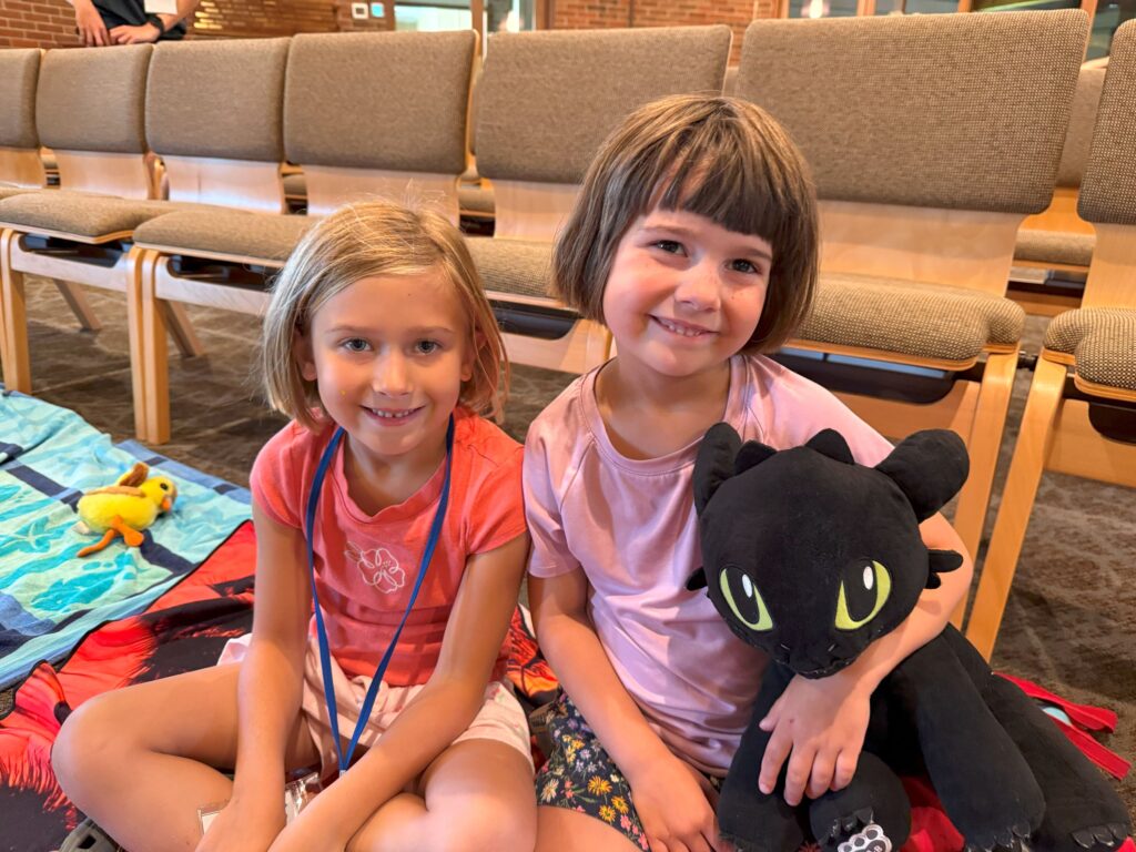 Two young girls sit beaming during Vacation Bible School.