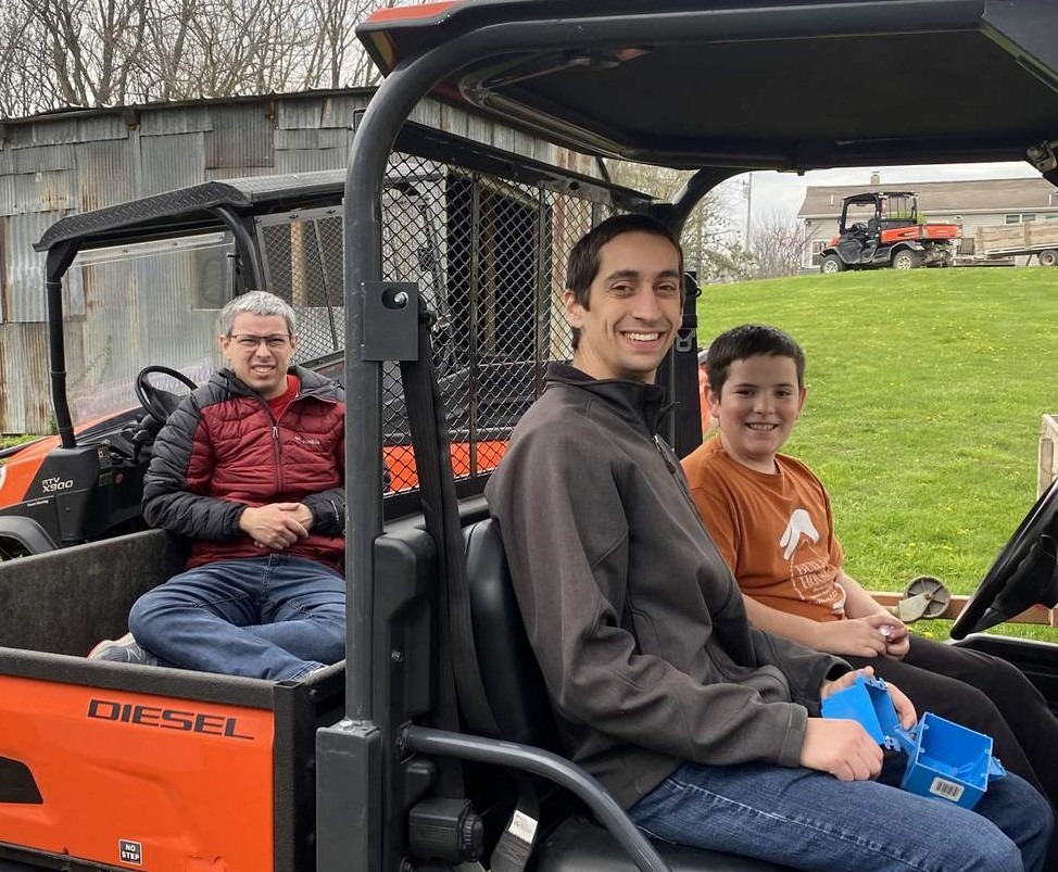 Two young men ride a golf cart with a boy at a Christian camp.
