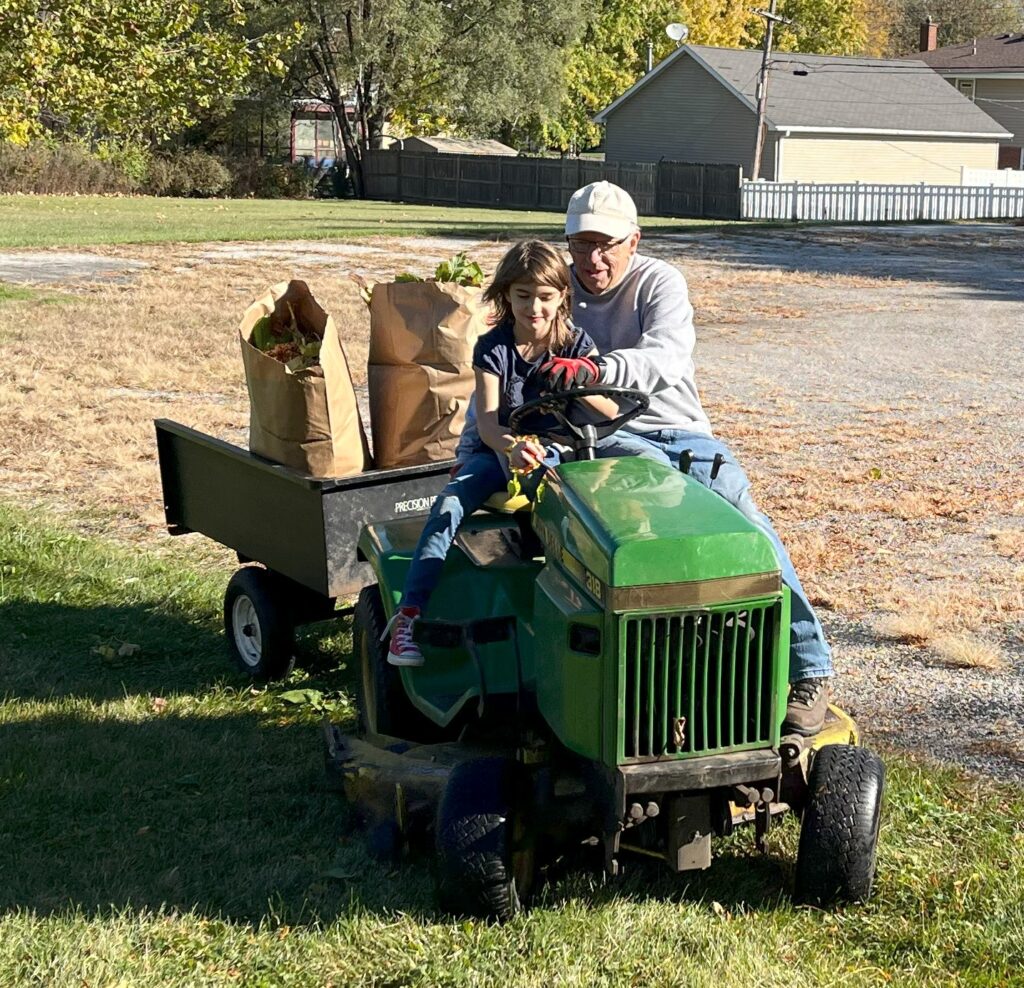 A man teaches a young girl to drive a tractor on a church lawn.