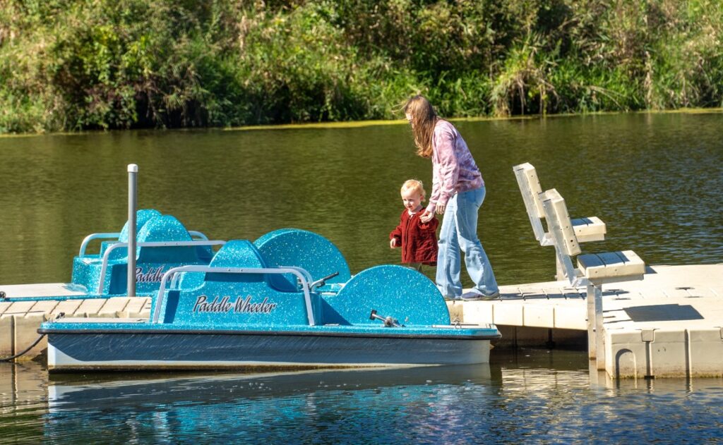 A teen guides a toddler along a boat dock in a lake.