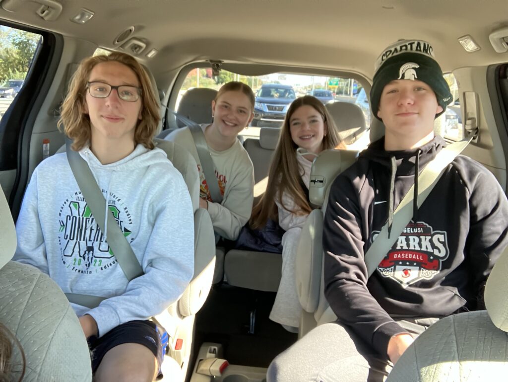 Four teens (two boys and two girls) smile within a mini-van. 