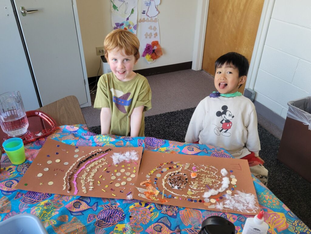 Two preschoolers show off their craft projects in a classroom.