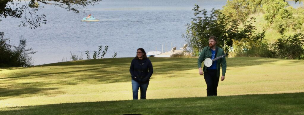 A woman and man walk up a grassy slope in front of a lake at a camp and retreat center.
