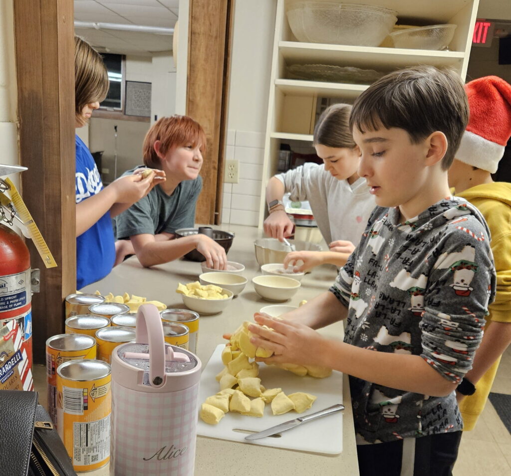 Several tween boys and a girl shaping biscuit dough around a counter in a church kitchen. 