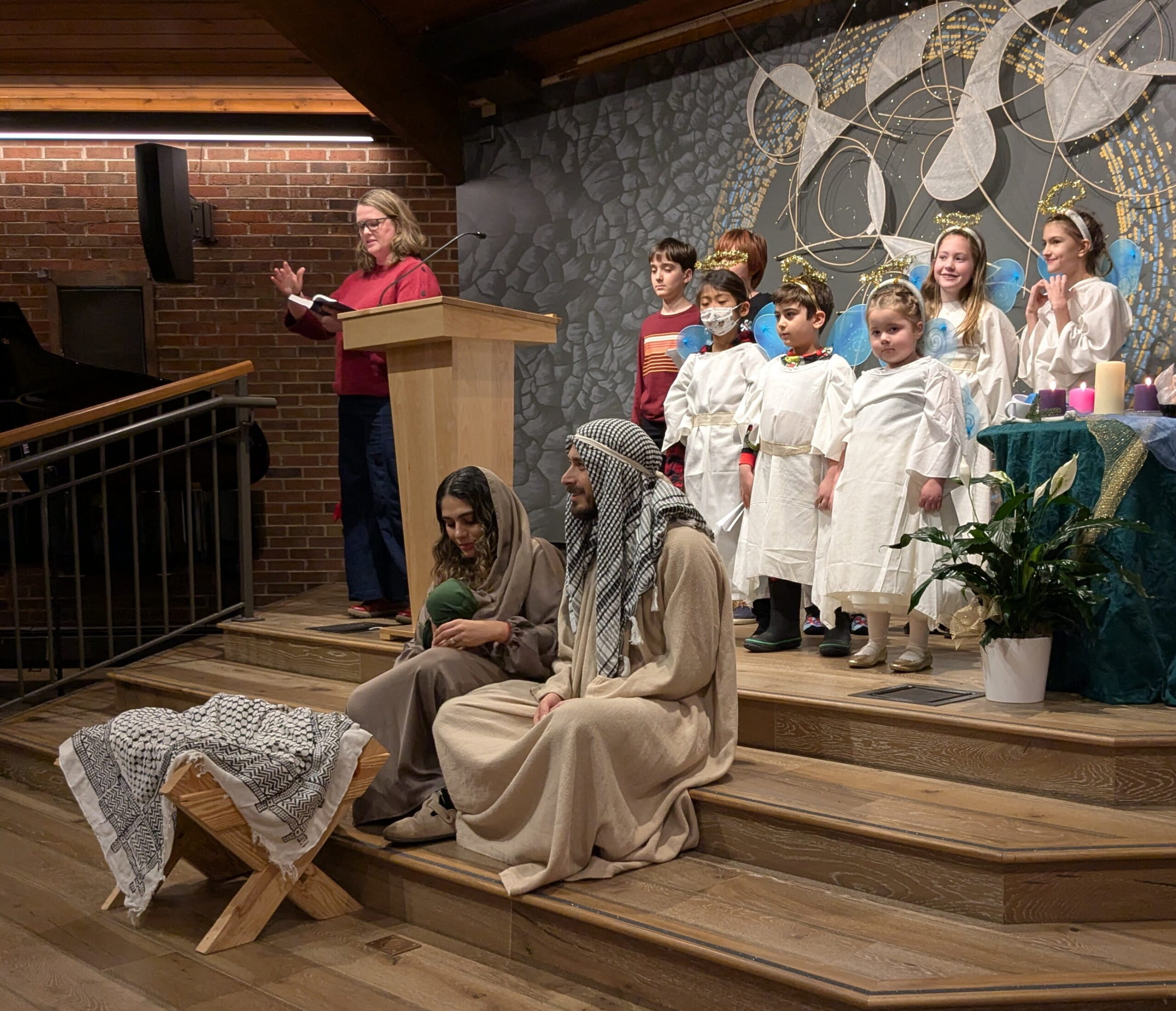 A nativity scene with two adults dressed as Mary and Joseph and several children dressed as angels, inside a church sanctuary. 