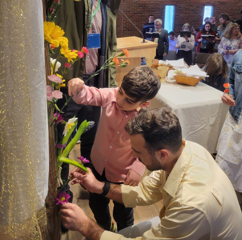A man and boy place flowers through a wire mesh around a wooden cross inside a church sanctuary. 