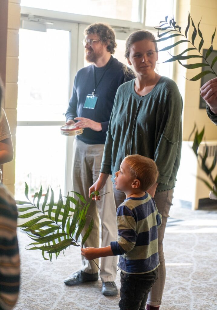 A woman and child hold palm branches in a church foyer, awaiting their turn in a Palm Sunday processional. 