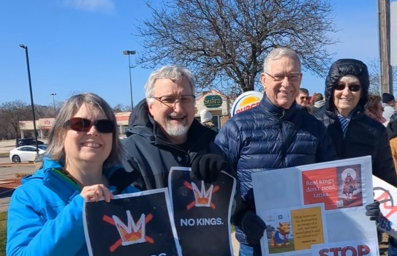 Two men and two women hold up protest signs at a No Kings rally.