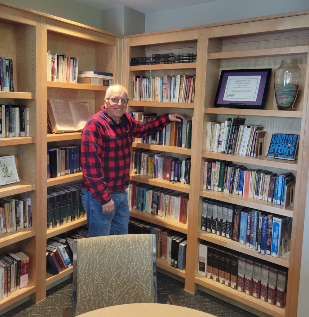 A man stands in front of bookshelves in a small library. 