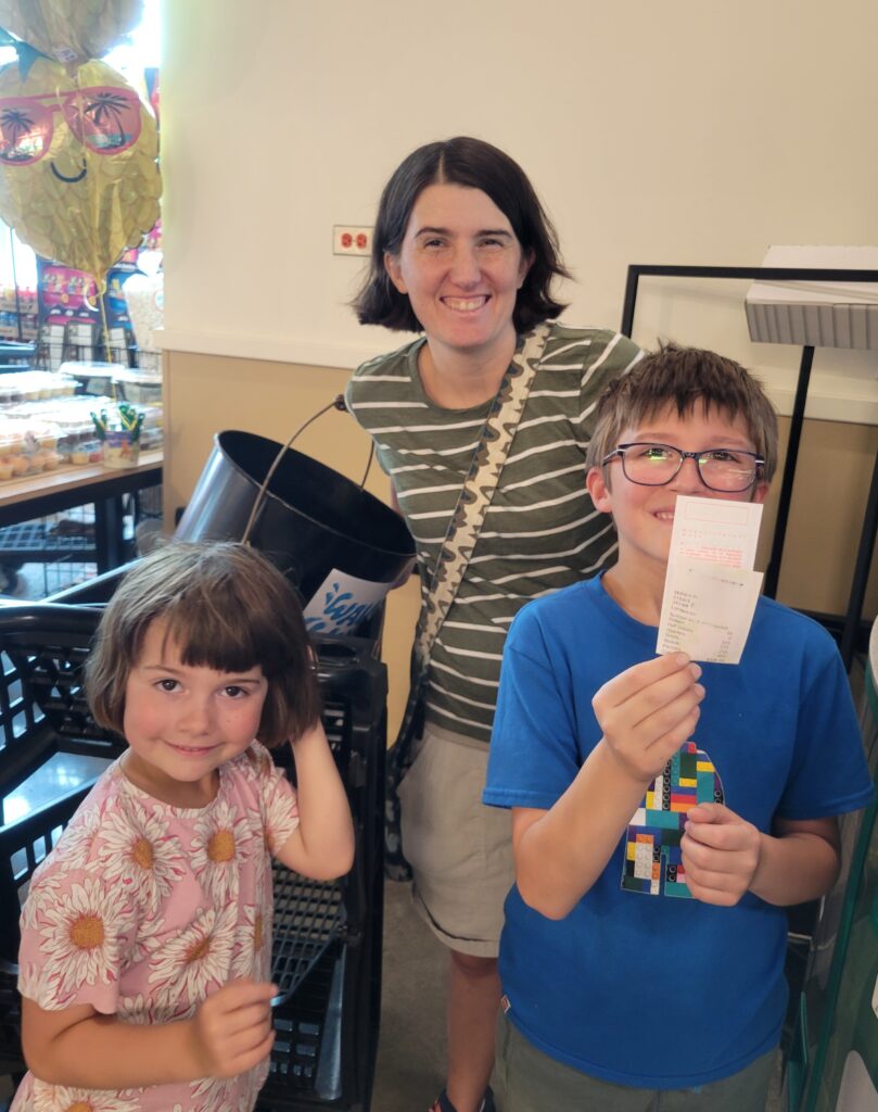 A woman and two children smile and pose with a receipt from a coin counting machine. 