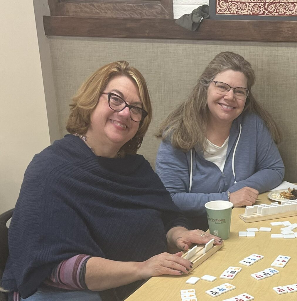 Two women smile as they play a game with tiles. 