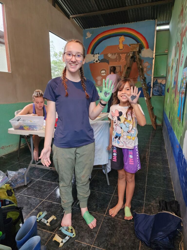 A teenage girl and a child show off paint covered hands after working on a Noah's Ark mural inside a Sunday school classroom.