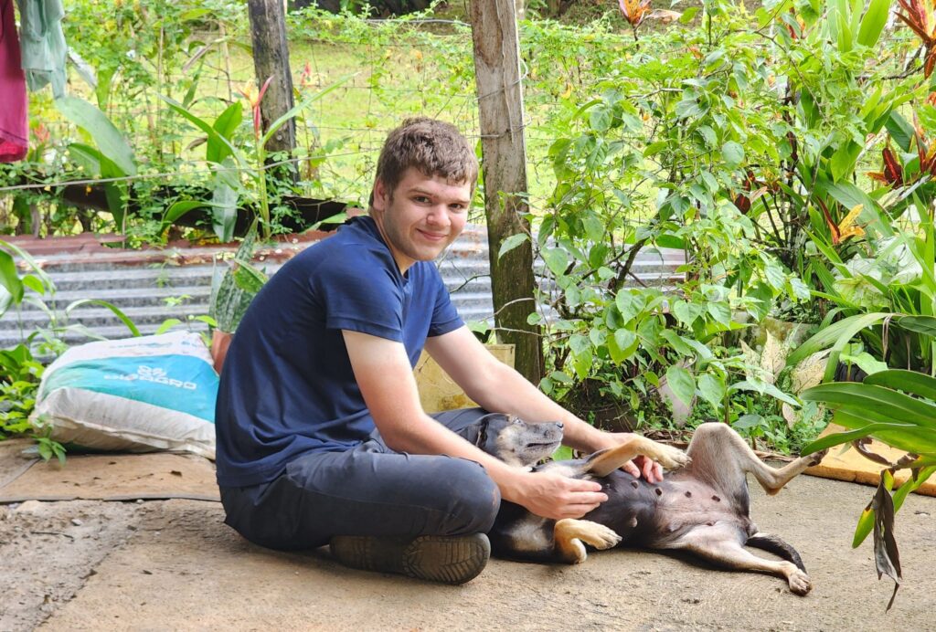 A teenager pets a dog in front of a green garden.
