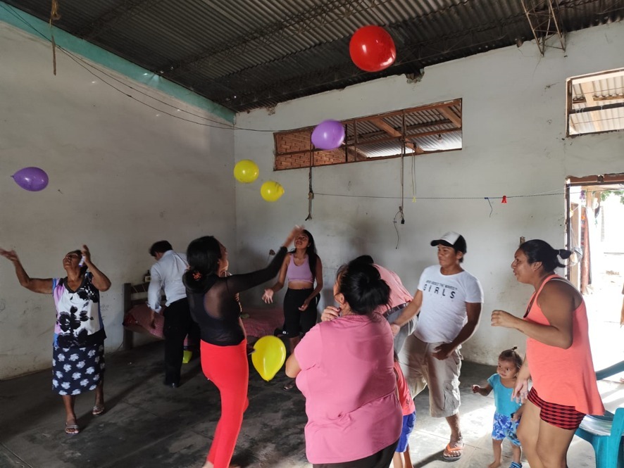 A group of men and women release balloons into the air inside a classroom.