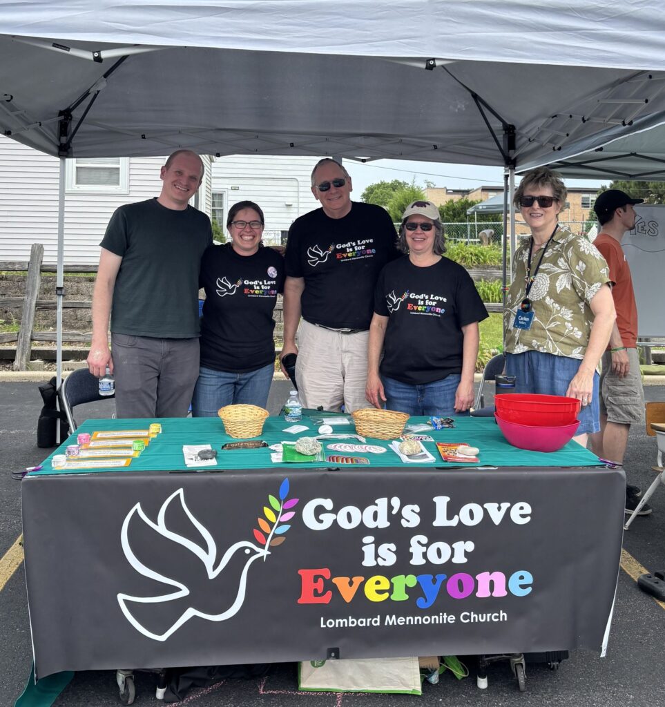 Five adults stand behind a table with a banner saying, "God's Love is for Everyone. Lombard Mennonite Church"