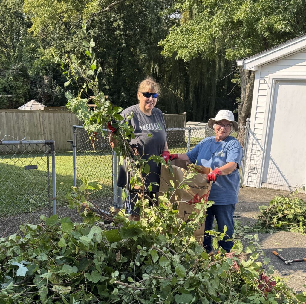 Two women bag branches and yard waste trimmed from trees.