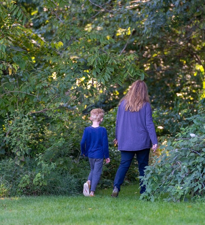 A mother and child walk into the woods.