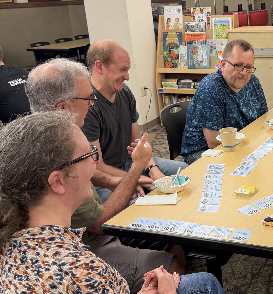 Group of adults smiling around a game table. 