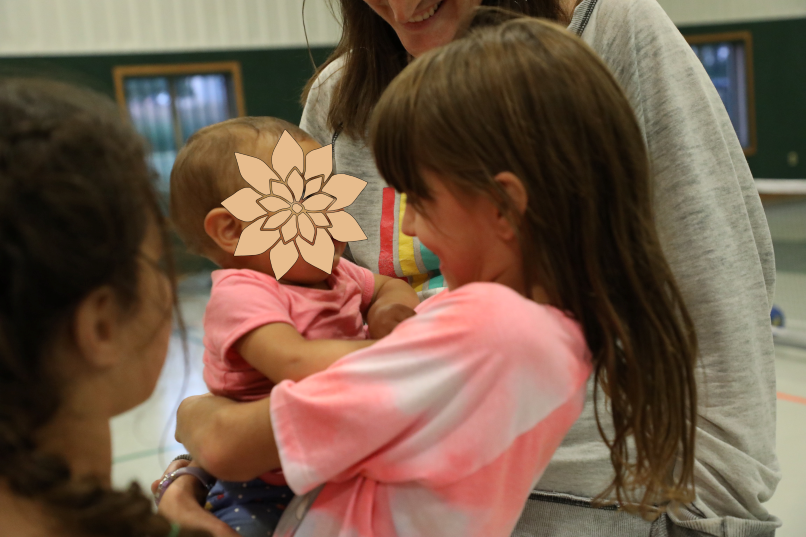 A smiling girl holds a baby inside a gym. 